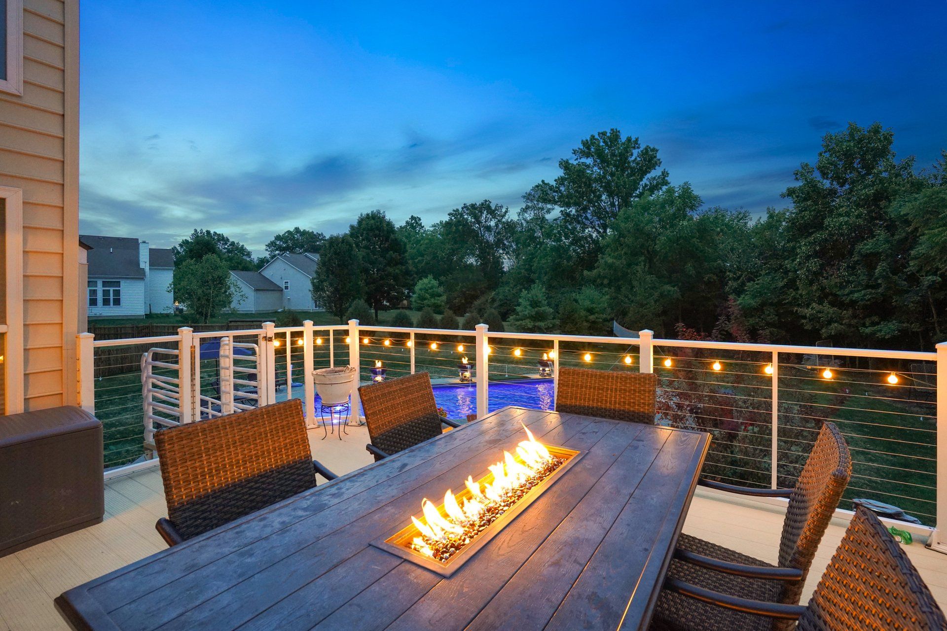 Deck with wicker chairs, fire pit, and string lights overlooking trees at dusk