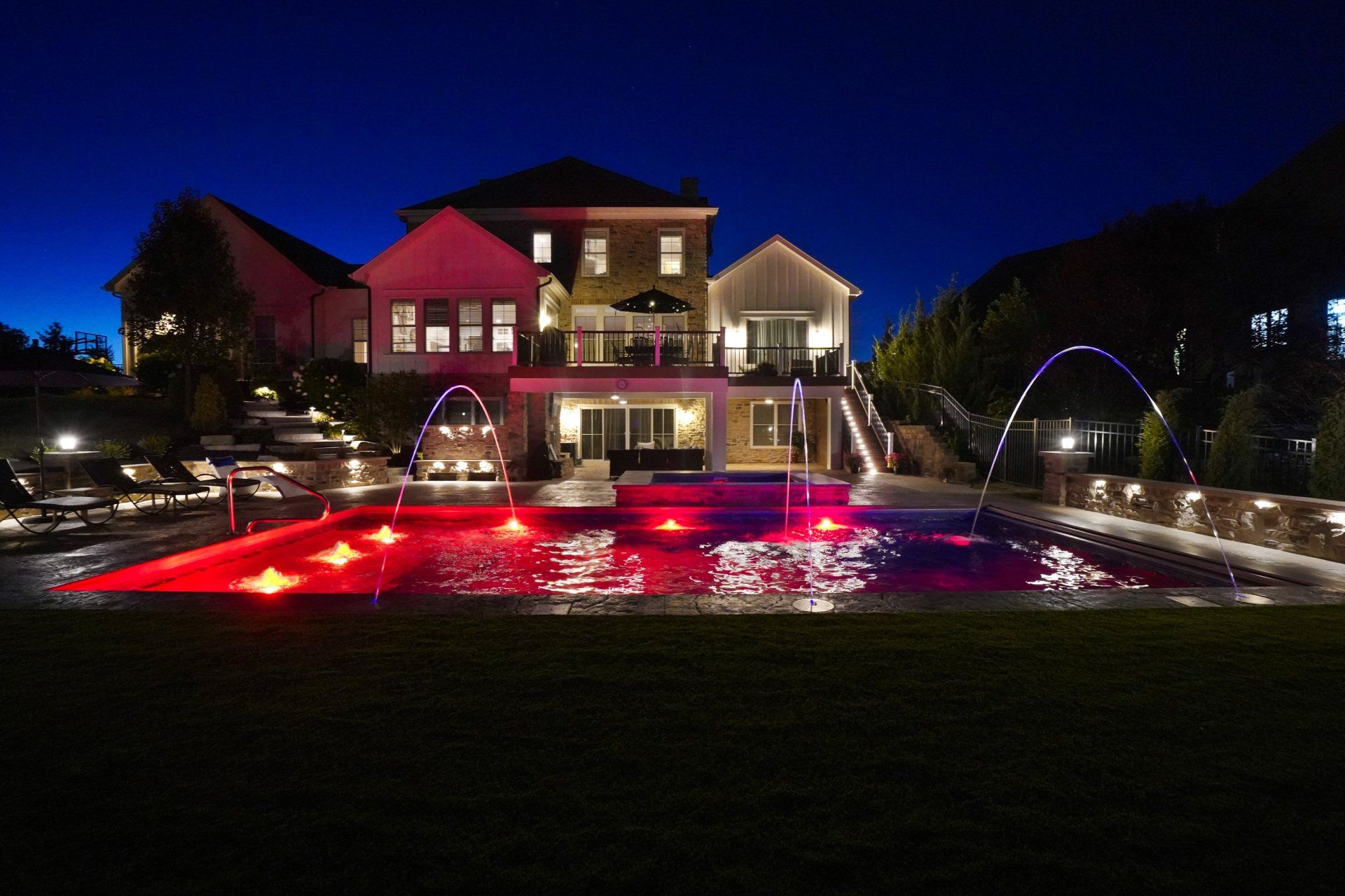 Large illuminated house with red-lit pool and arched water feature at night