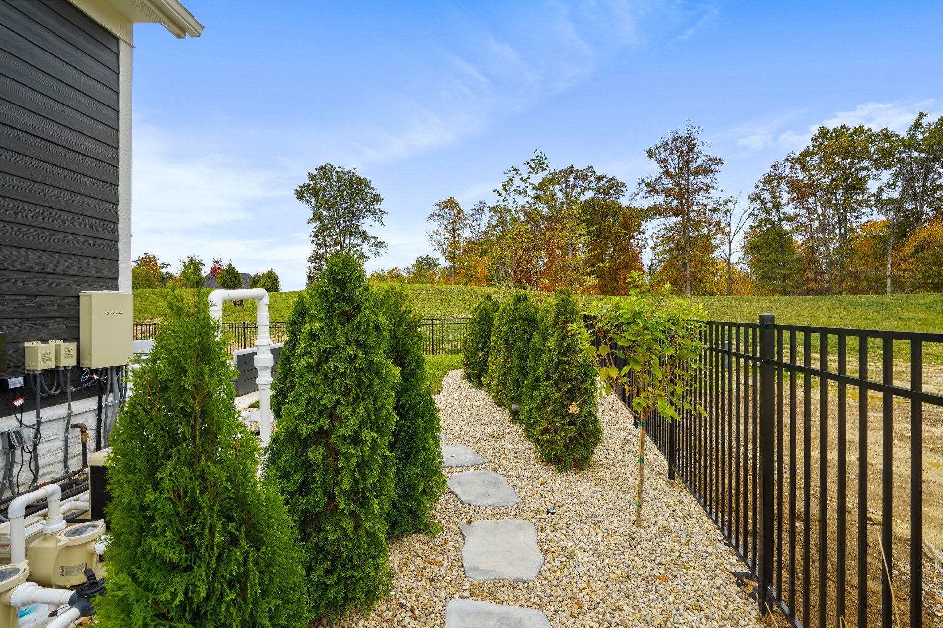 Stone path through gravel garden beside black fence and green shrubs next to a house.