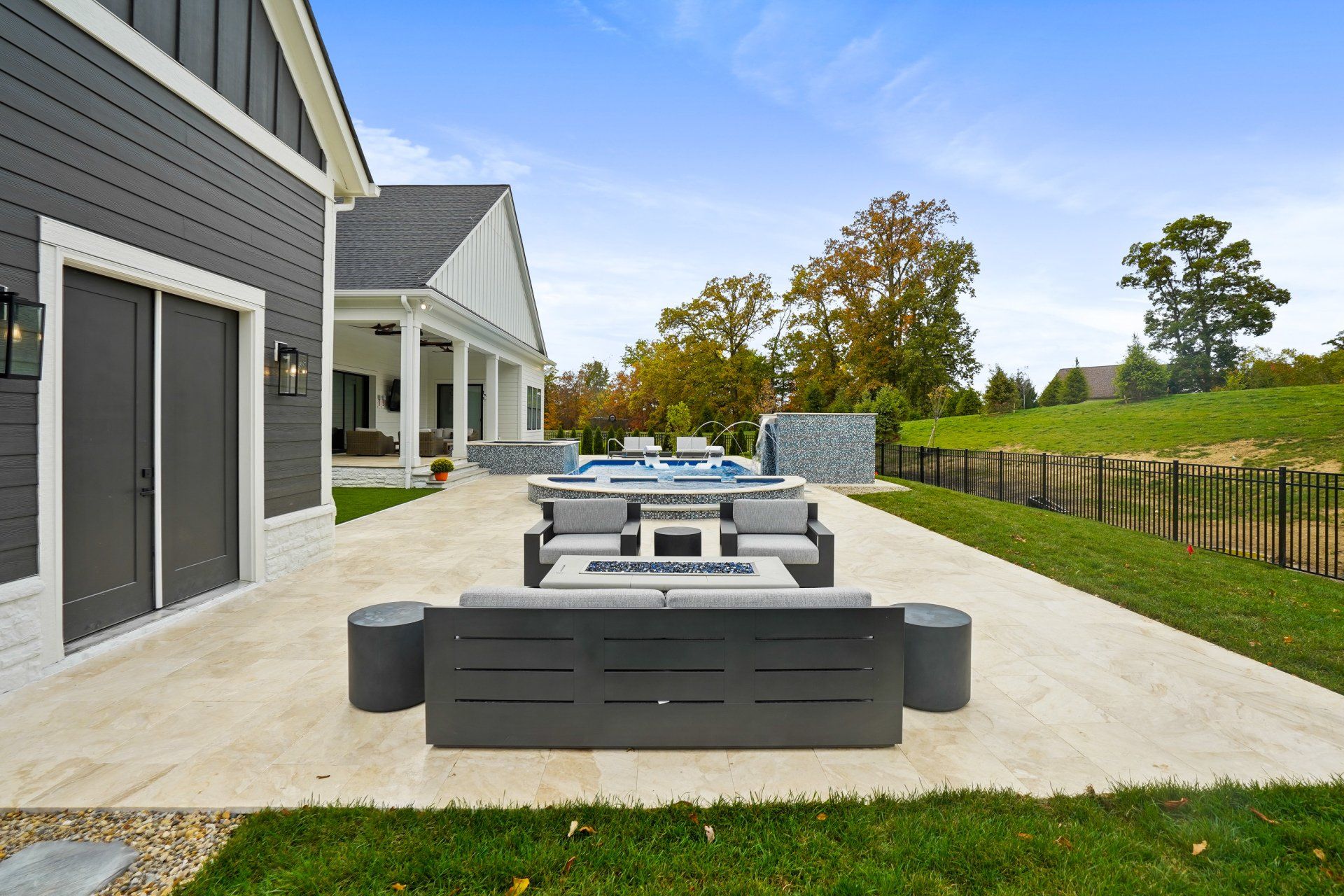 Modern backyard patio with outdoor dining set, gray house siding, and fenced lawn under overcast skies