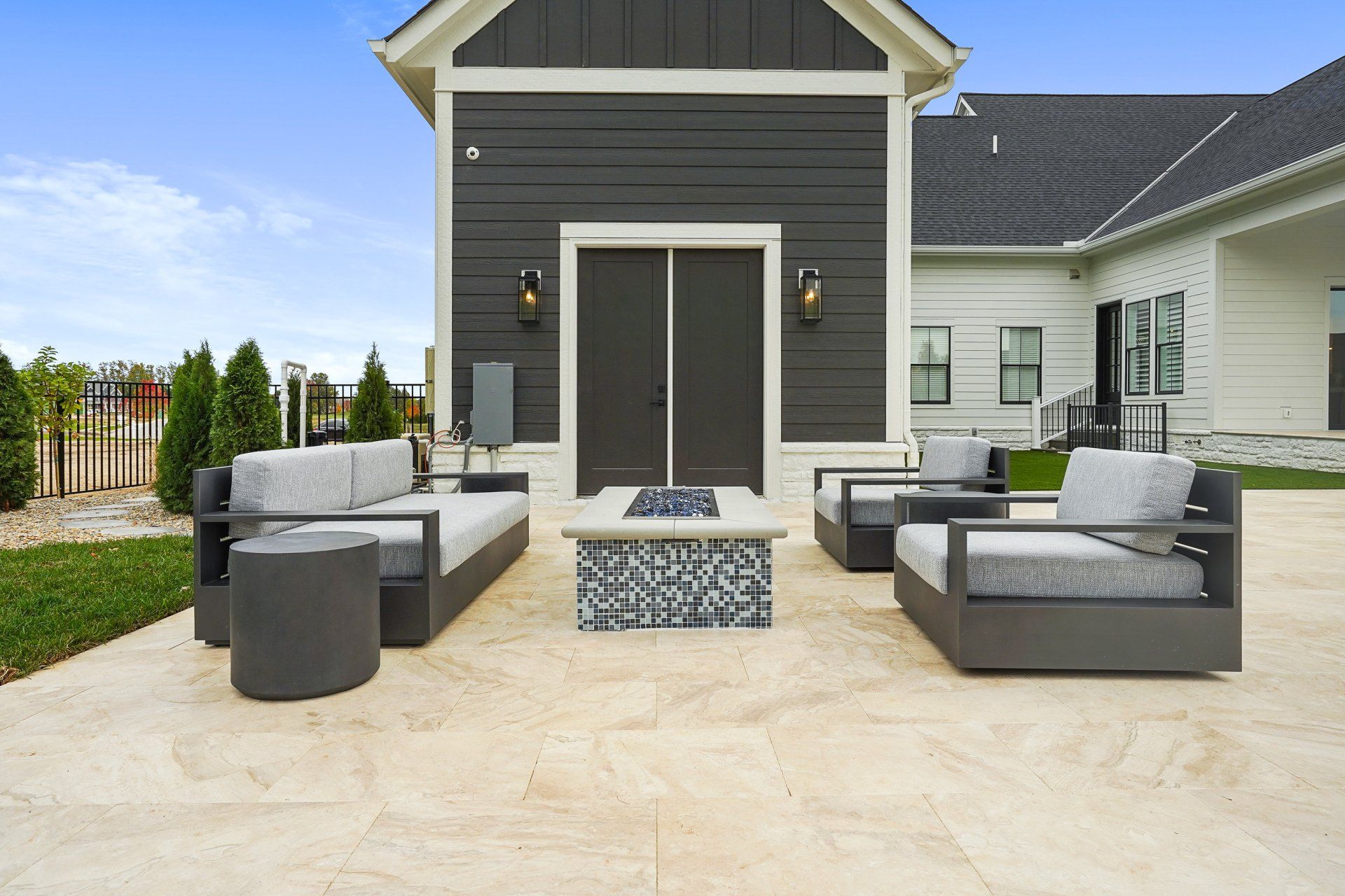 Outdoor patio with gray sectional seating, a fire pit, and double doors on a modern house