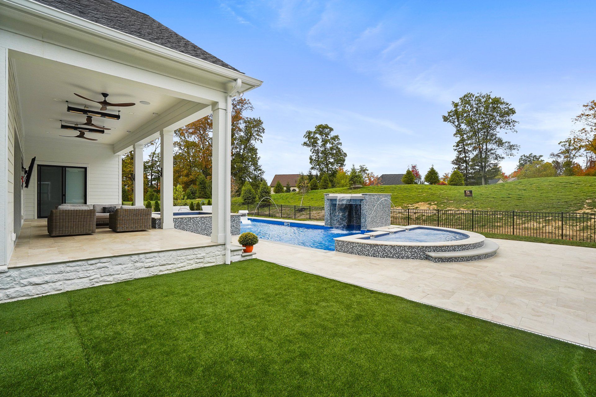 Patio and pool area beside a house, with green lawn, lounge seating, and a small waterfall feature