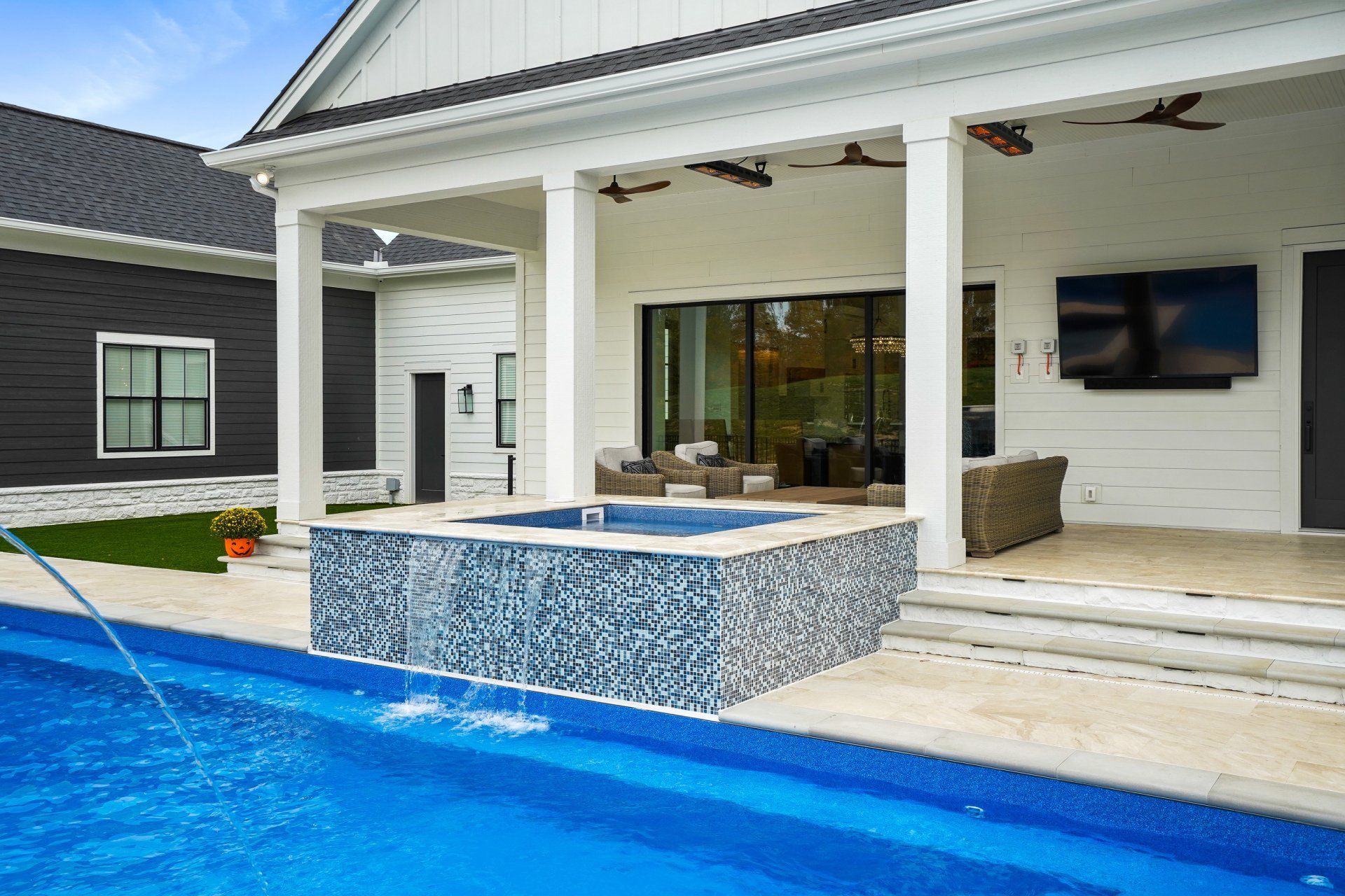 Modern backyard patio with blue pool, tiled spa, white columns, and covered outdoor seating area