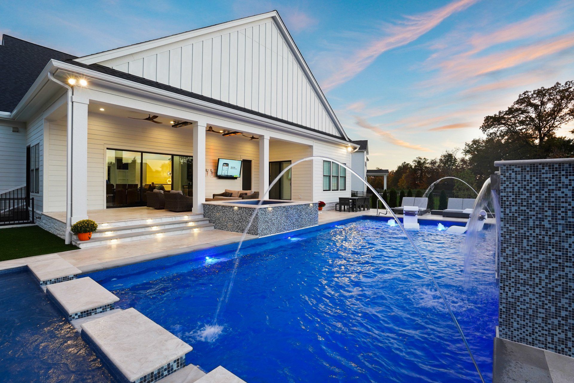 Modern white house with a covered patio overlooking a bright blue swimming pool at sunset