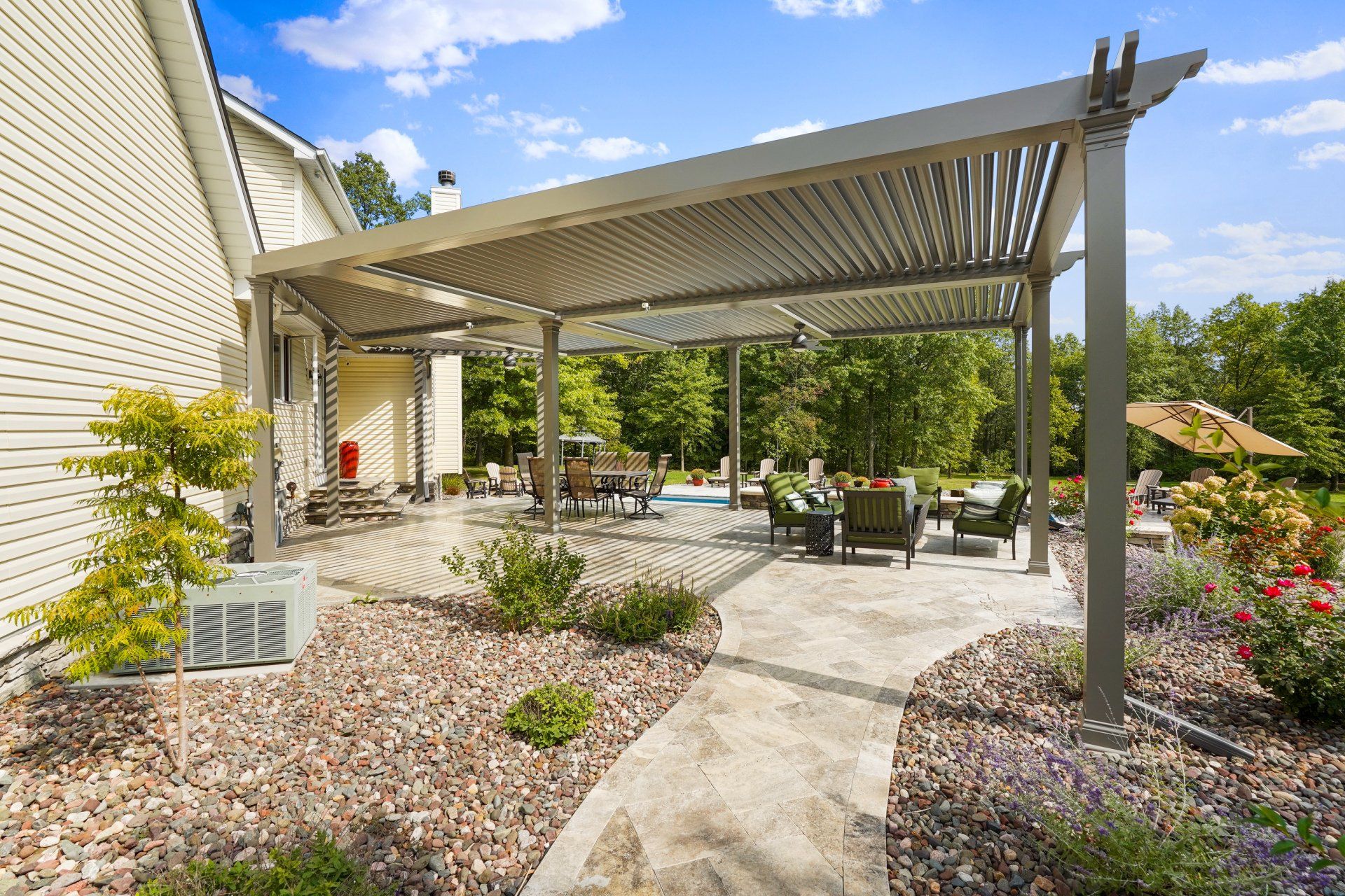 Covered patio with metal pergola, outdoor seating, and landscaped garden walkway beside a house