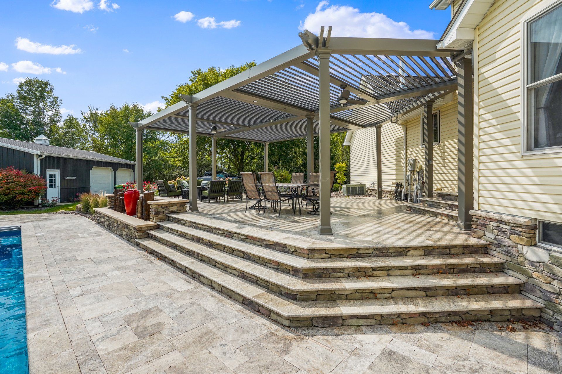 Backyard patio with pergola, outdoor dining table, and stone steps beside a house and pool.