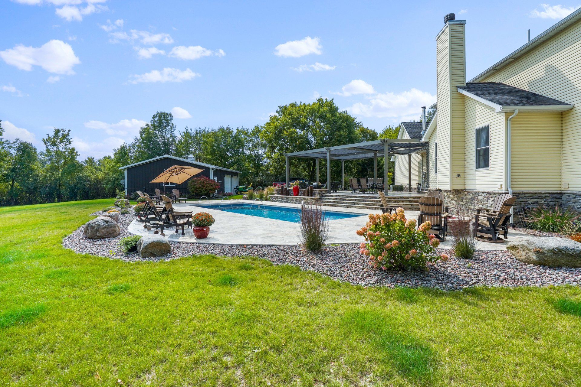 Backyard patio with in-ground pool, stone landscaping, umbrella seating, and a house