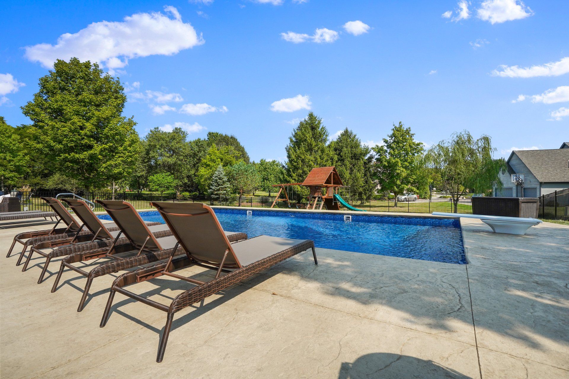 Outdoor pool with lounge chairs, blue water, and trees under a sunny sky