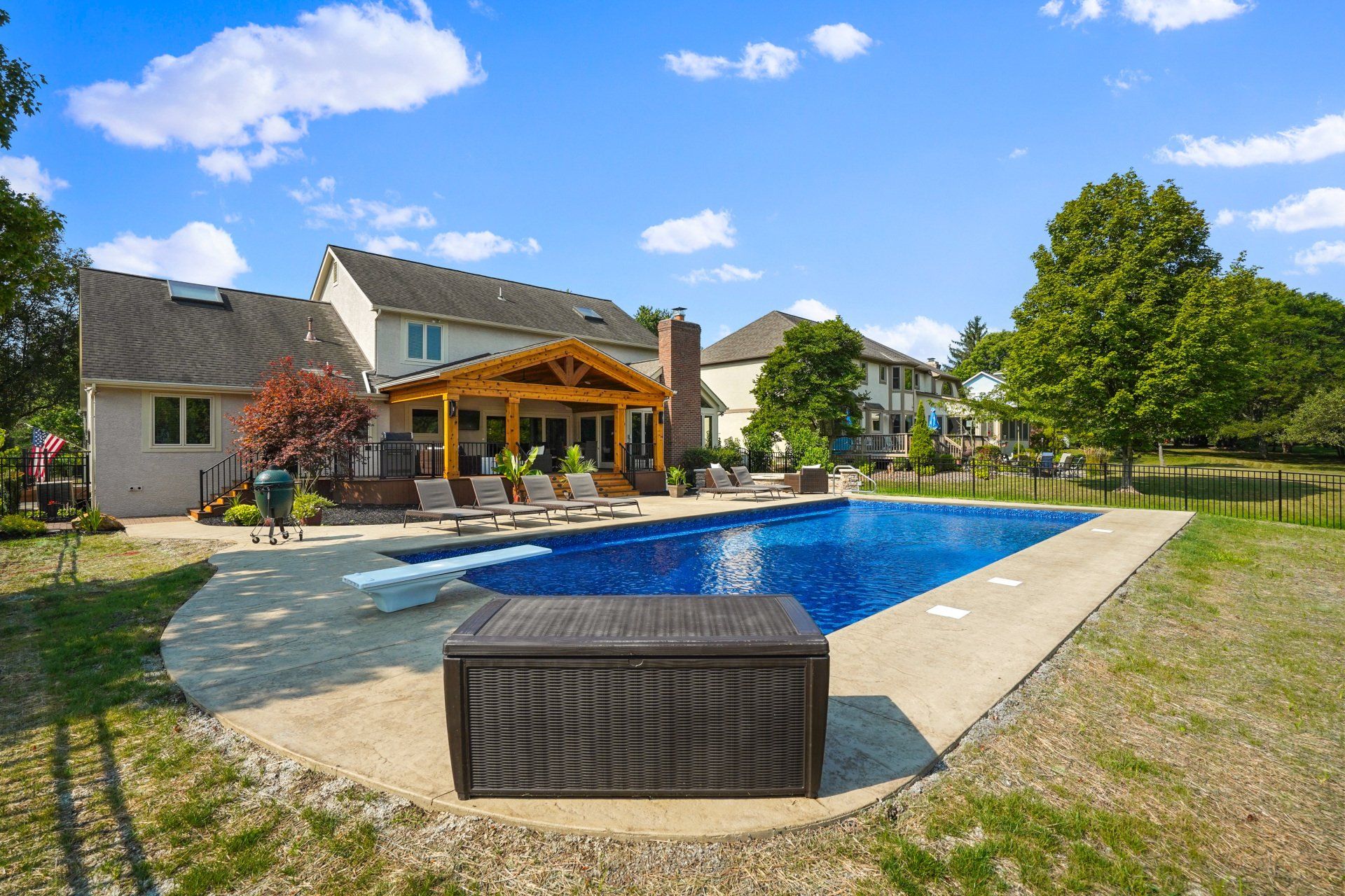 Backyard with a blue swimming pool, patio, and house under a sunny sky