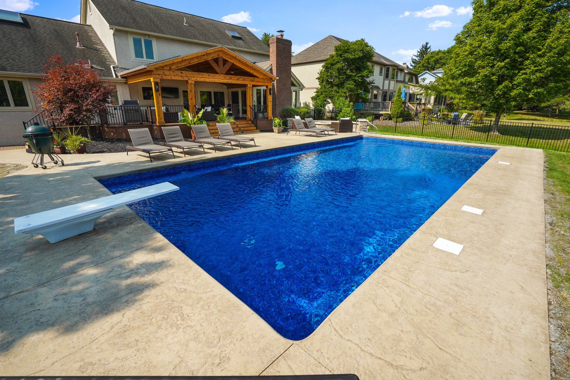 Backyard swimming pool beside a covered patio and lounge chairs on a sunny day