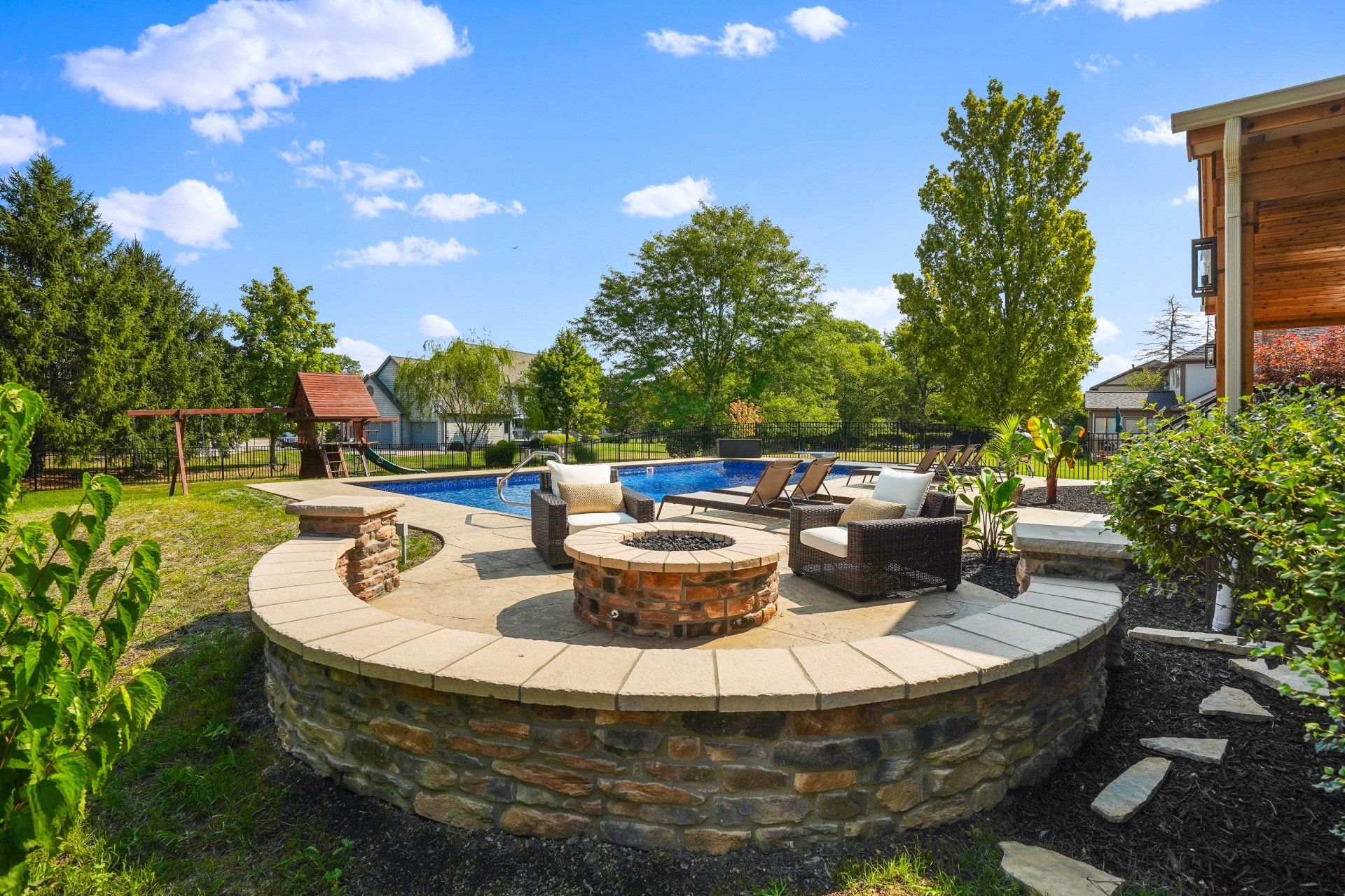 Patio seating around a fire pit beside a pool under a blue sky