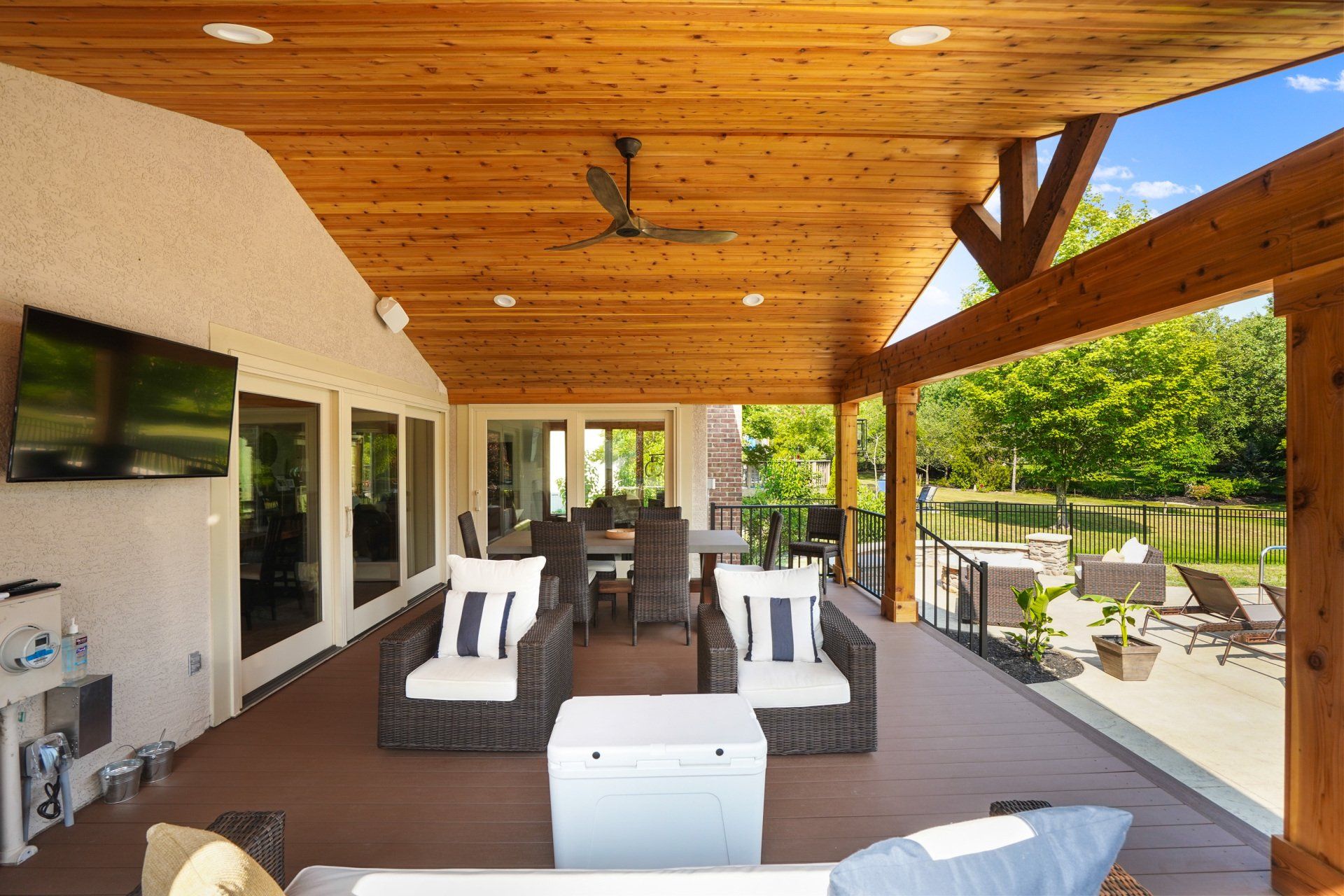 Covered patio with wicker seating, wall-mounted TV, and a view of the backyard garden.