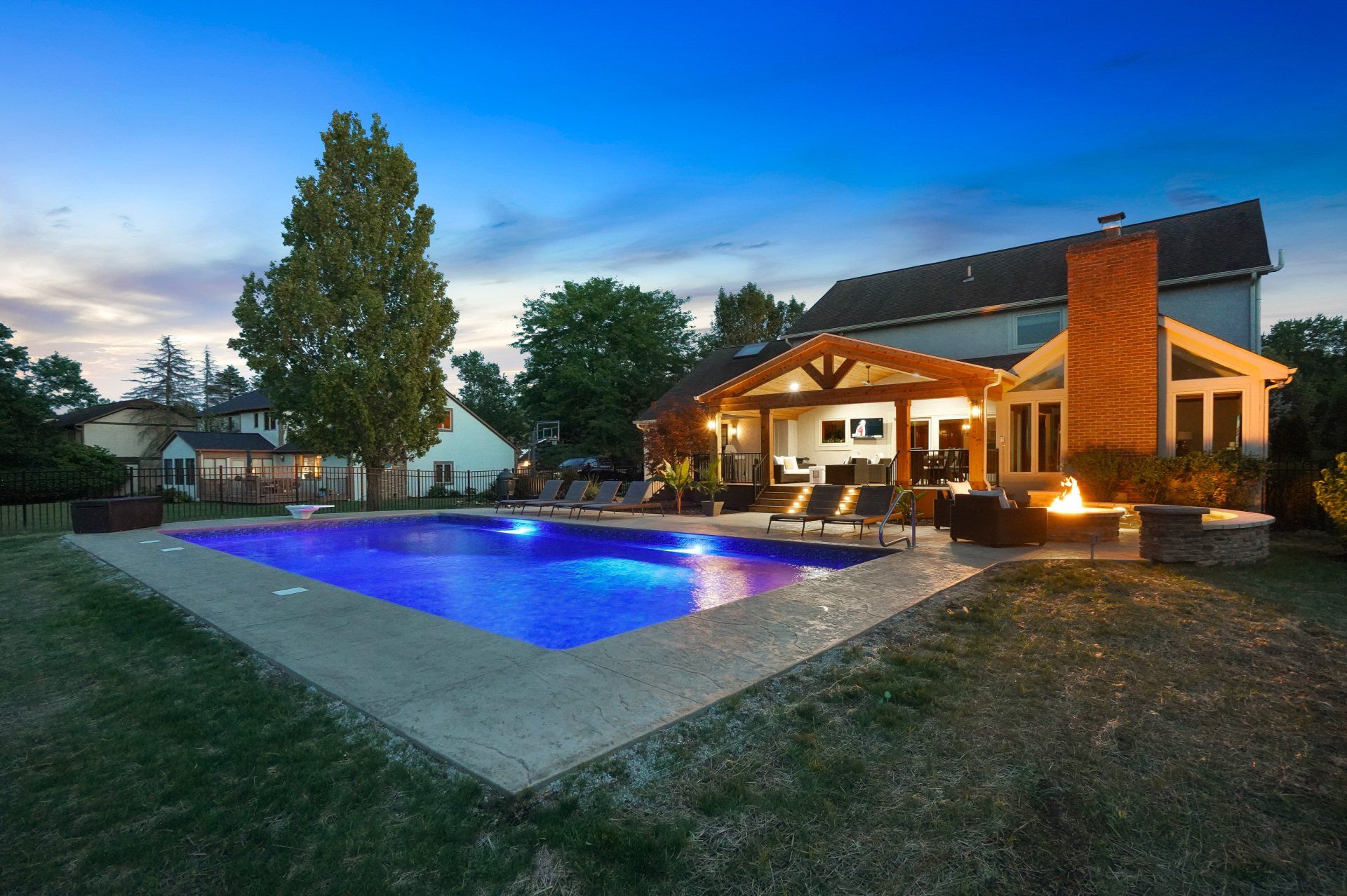 Modern house with a lit blue swimming pool at dusk in a backyard.