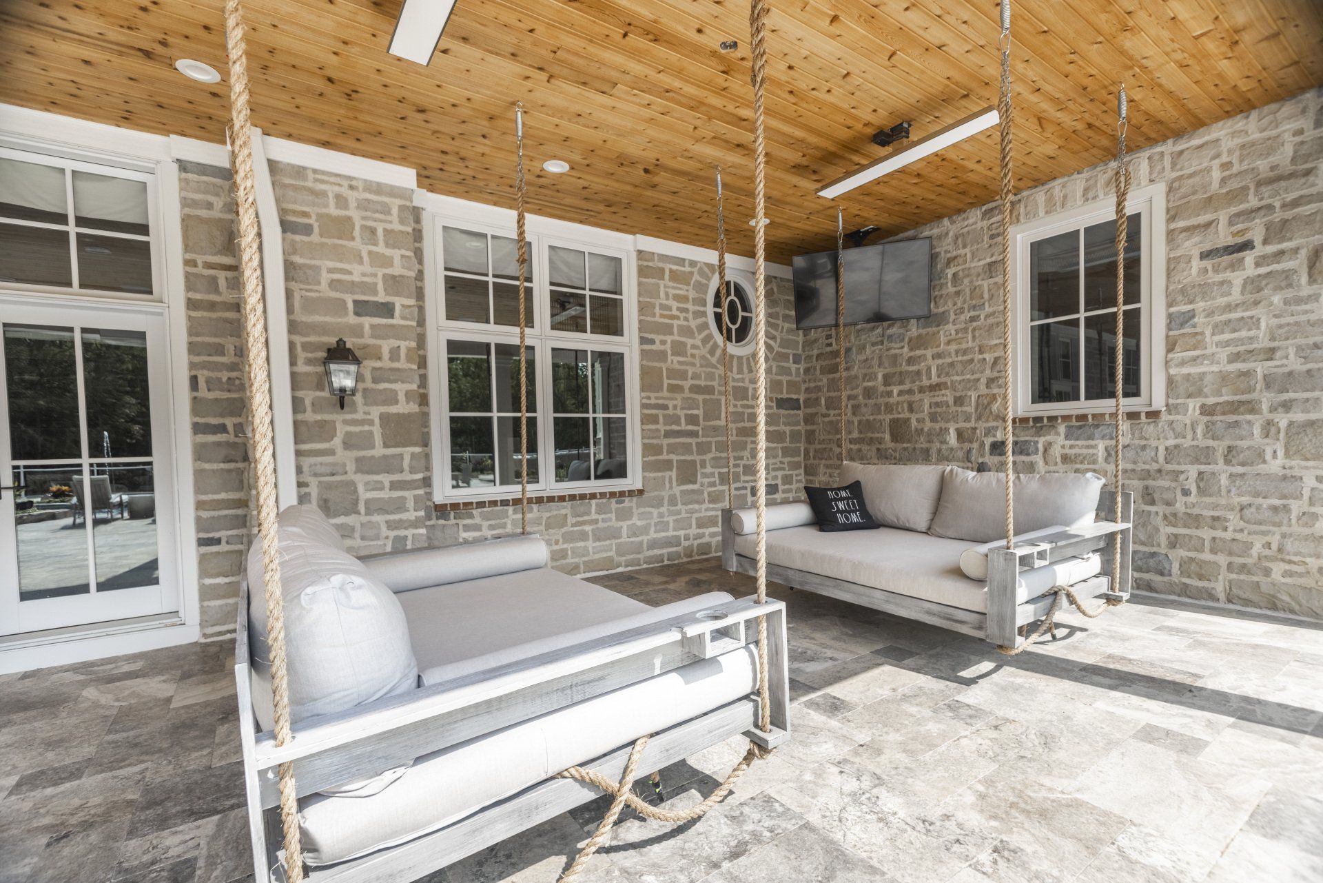 Stone porch with hanging daybeds, white cushions, and a wooden ceiling, lit by sunlight