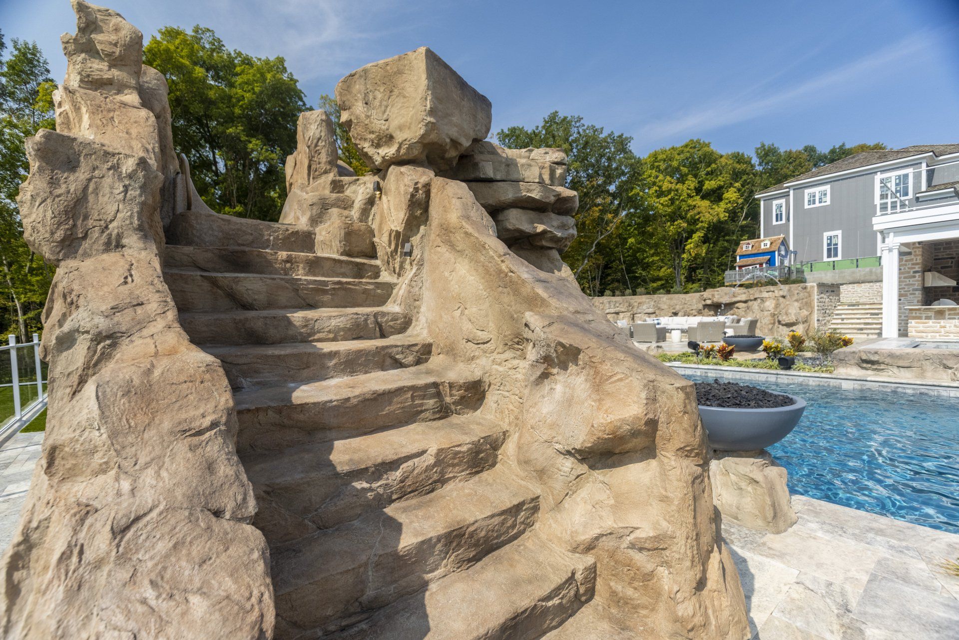 Rock-like staircase beside a blue pool, with trees and a building in the background