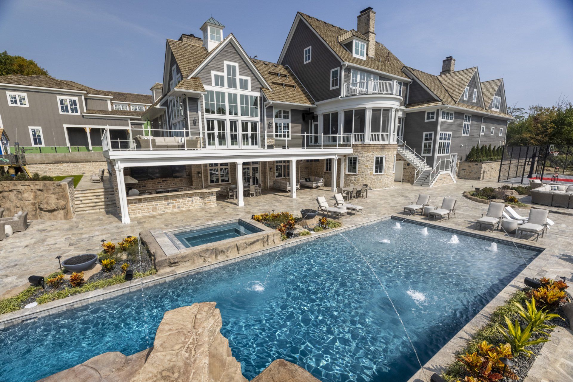 Luxury stone mansion with a large blue pool and hot tub in a landscaped backyard