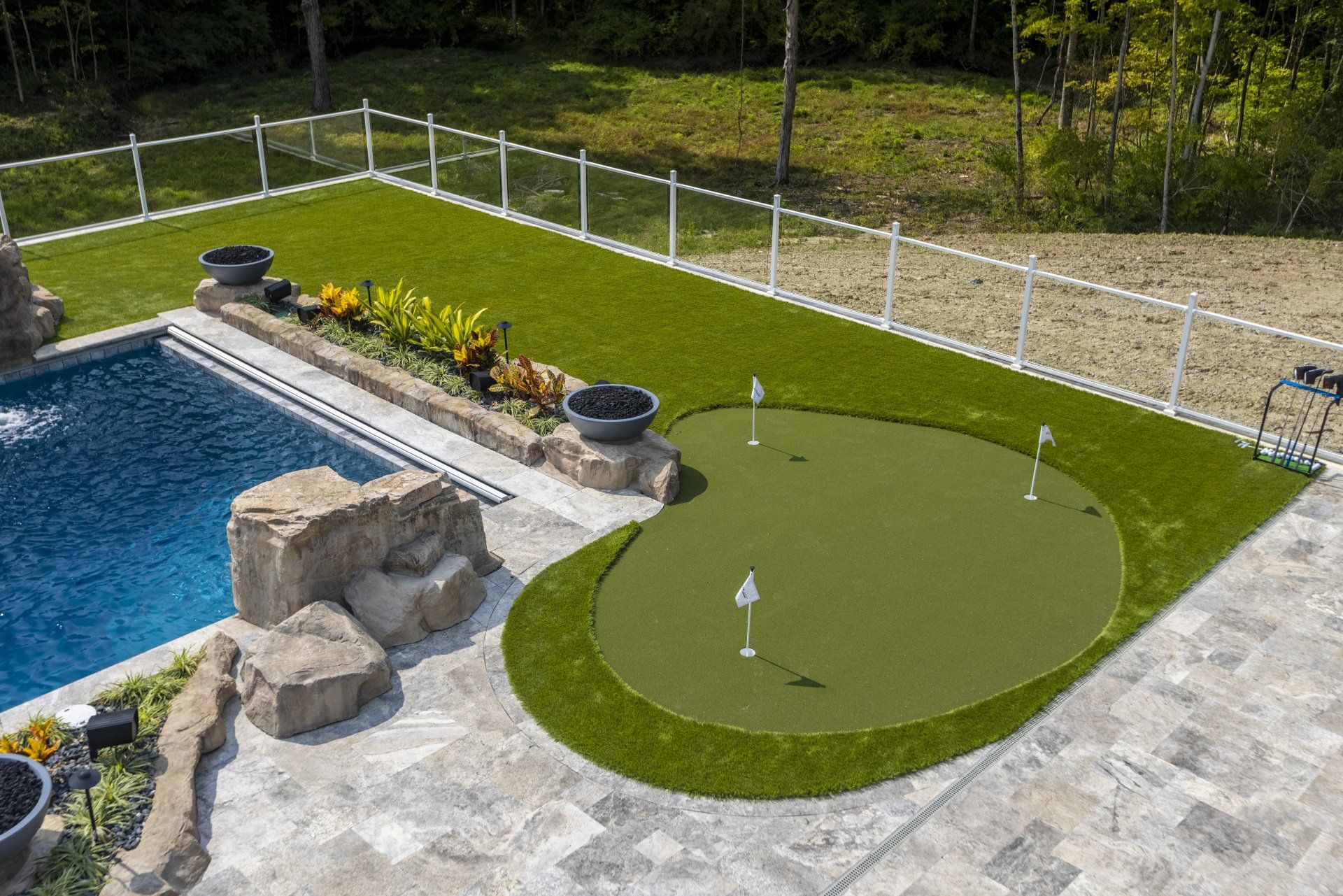 Backyard pool with stone features, green lawn putting area, and fenced grassy yard