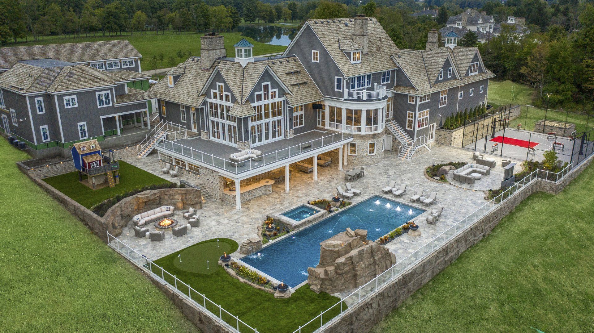 Aerial view of a large stone mansion with a pool, patio, and manicured lawn by the water.