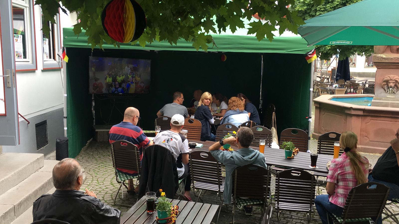 Eine Gruppe von Leuten sitzt an Tischen unter einem Sonnenschirm.