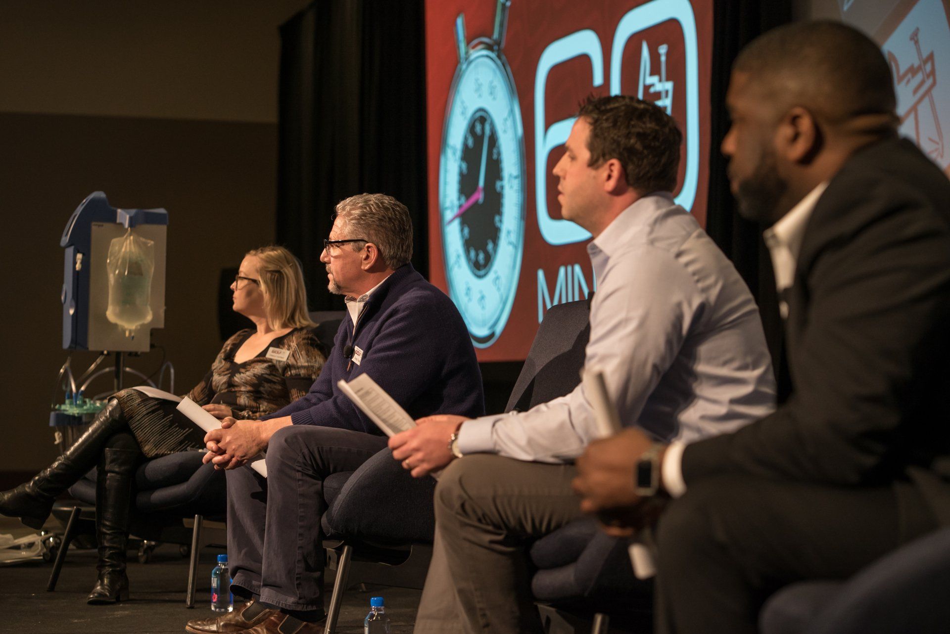 A group of people are sitting in chairs in front of a screen with a clock on it.