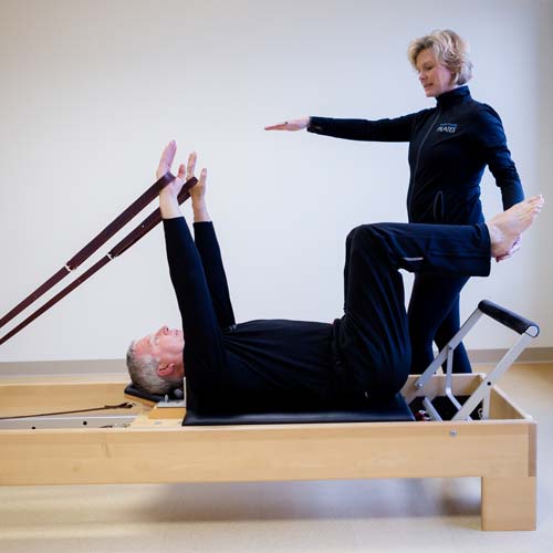 A woman is standing next to a man on a pilates machine