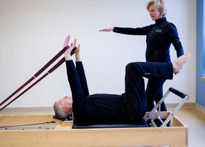 A woman is helping a man do exercises on a pilates machine.
