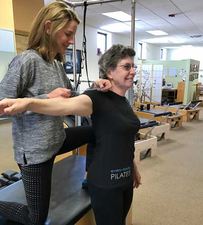 A woman is helping another woman stretch her arm in a gym.