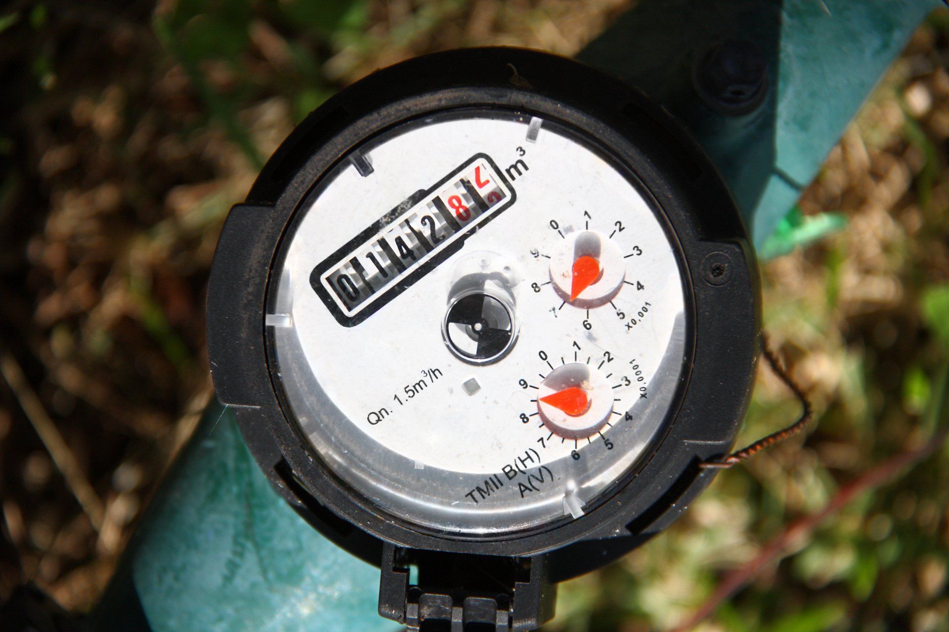 A close up of a water meter on a green pipe.