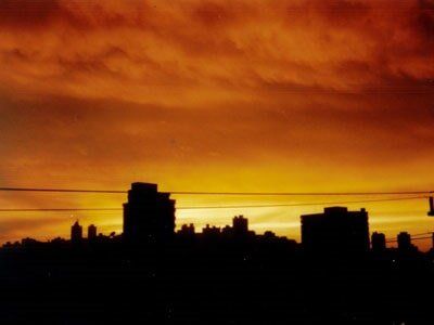 Silhouette of city buildings against a vibrant orange and yellow sunset.