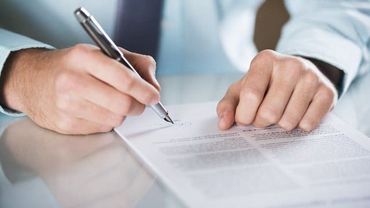 Ein Mann schreibt mit einem Stift auf ein Blatt Papier.