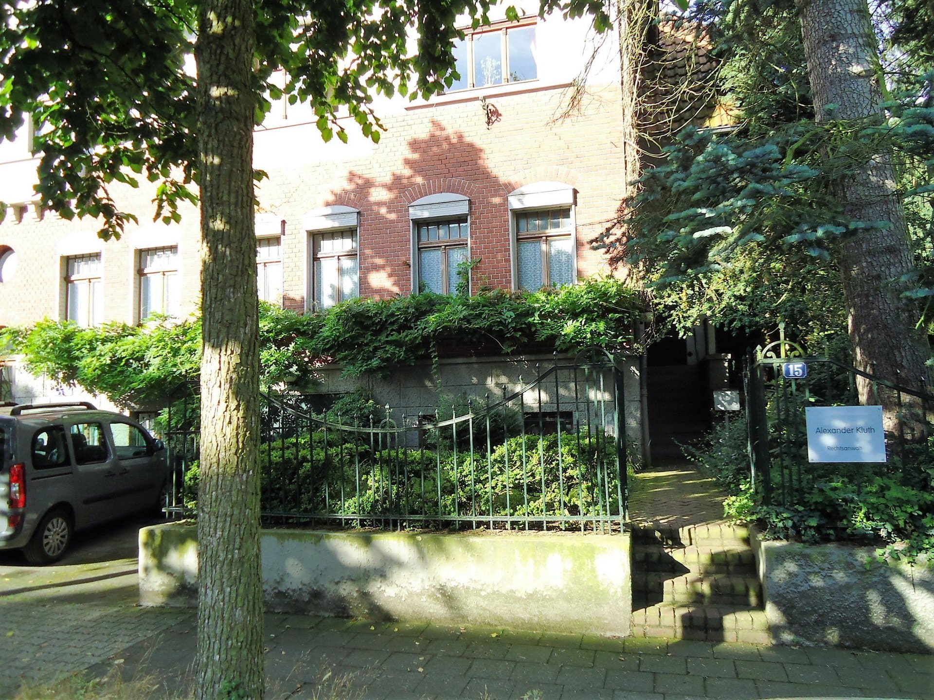 Ein Backsteingebäude mit einem Baum davor und einem davor geparkten Auto.