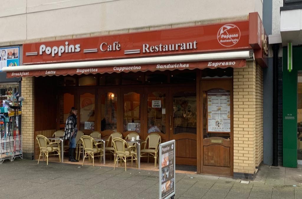 Poppins Cafe Restaurant storefront with outdoor seating and red awning on a street corner