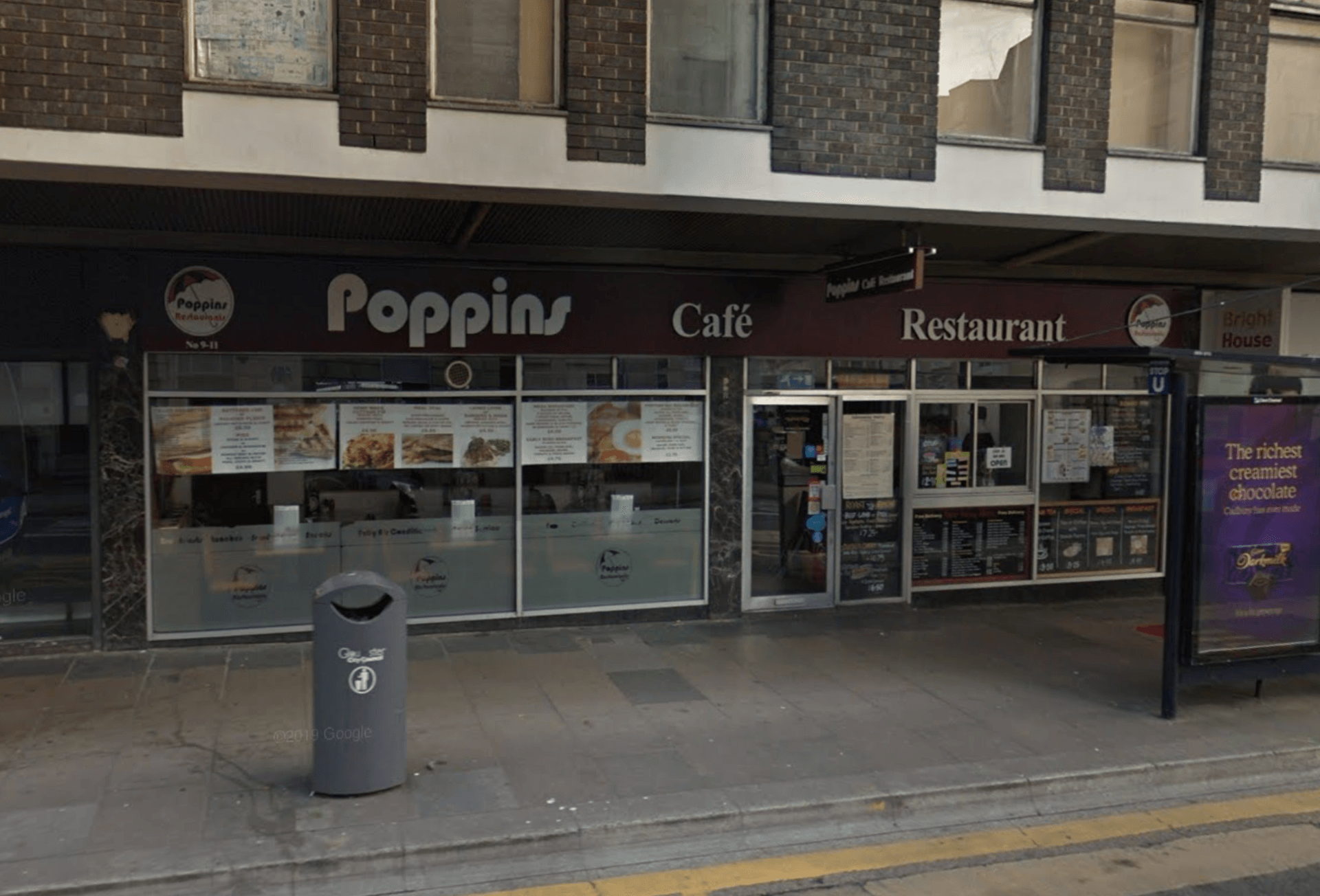 Storefront of Poppin Cafe Restaurant with glass windows, sidewalk bin, and bus stop sign outside