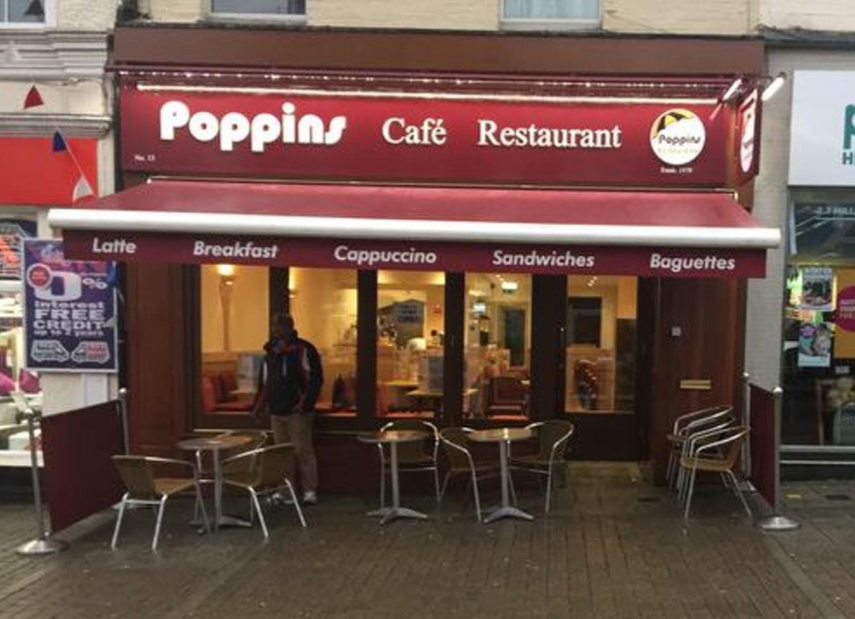 Poppin’s Café Restaurant storefront with red awning and outdoor seating on a rainy street