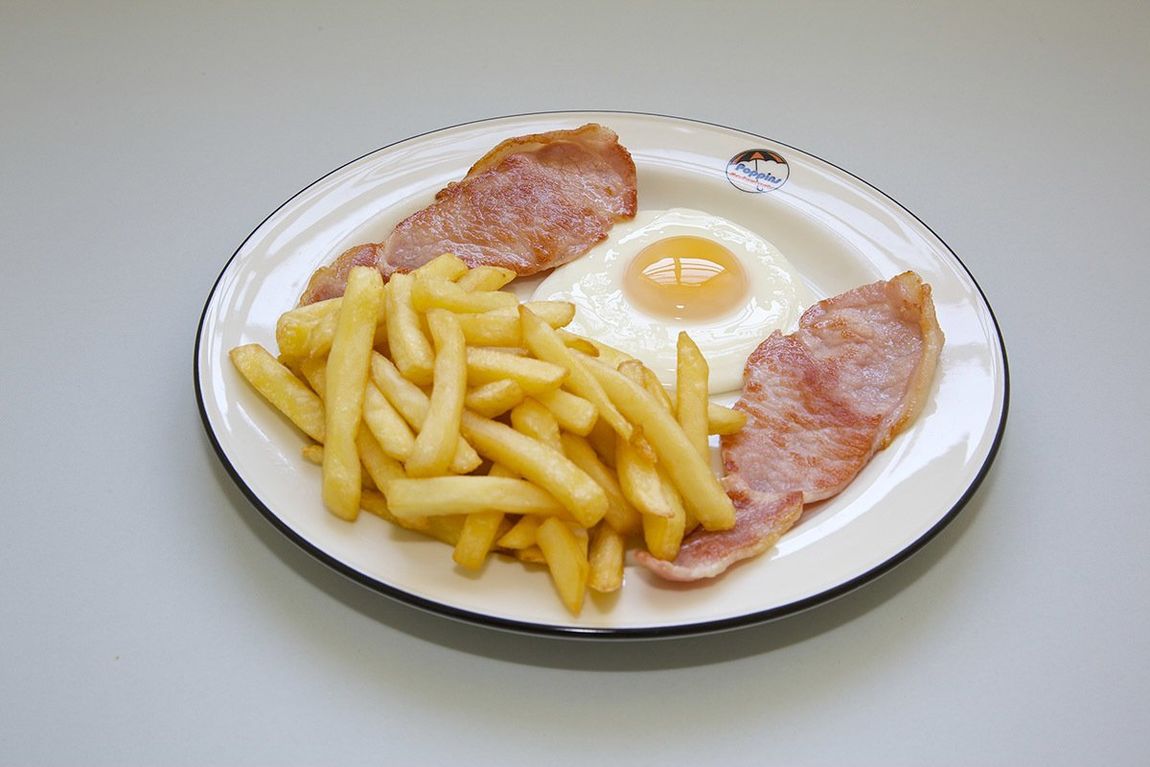 Plate with French fries, two slices of bacon, and a fried egg on a white dish