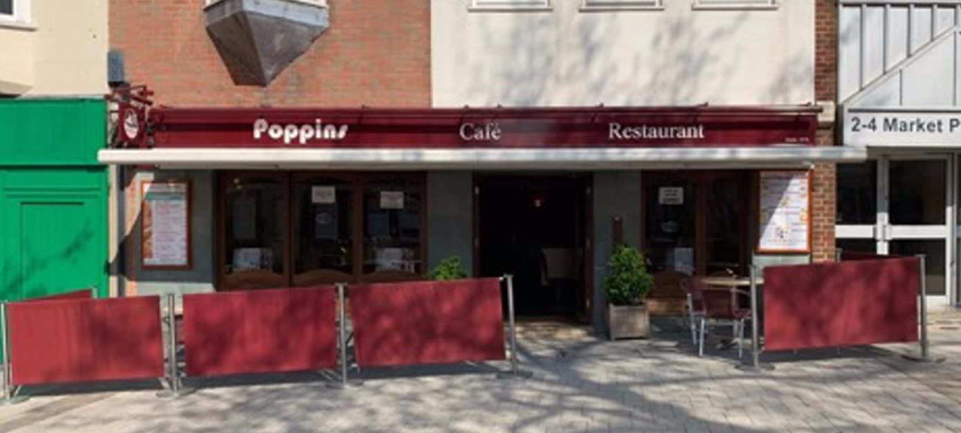 Outdoor café storefront with red awning and red patio barriers on a city sidewalk