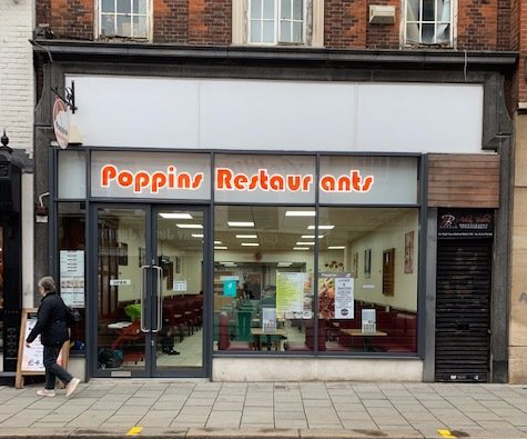 Storefront of Poppins Restaurant with orange sign and glass front on a city sidewalk
