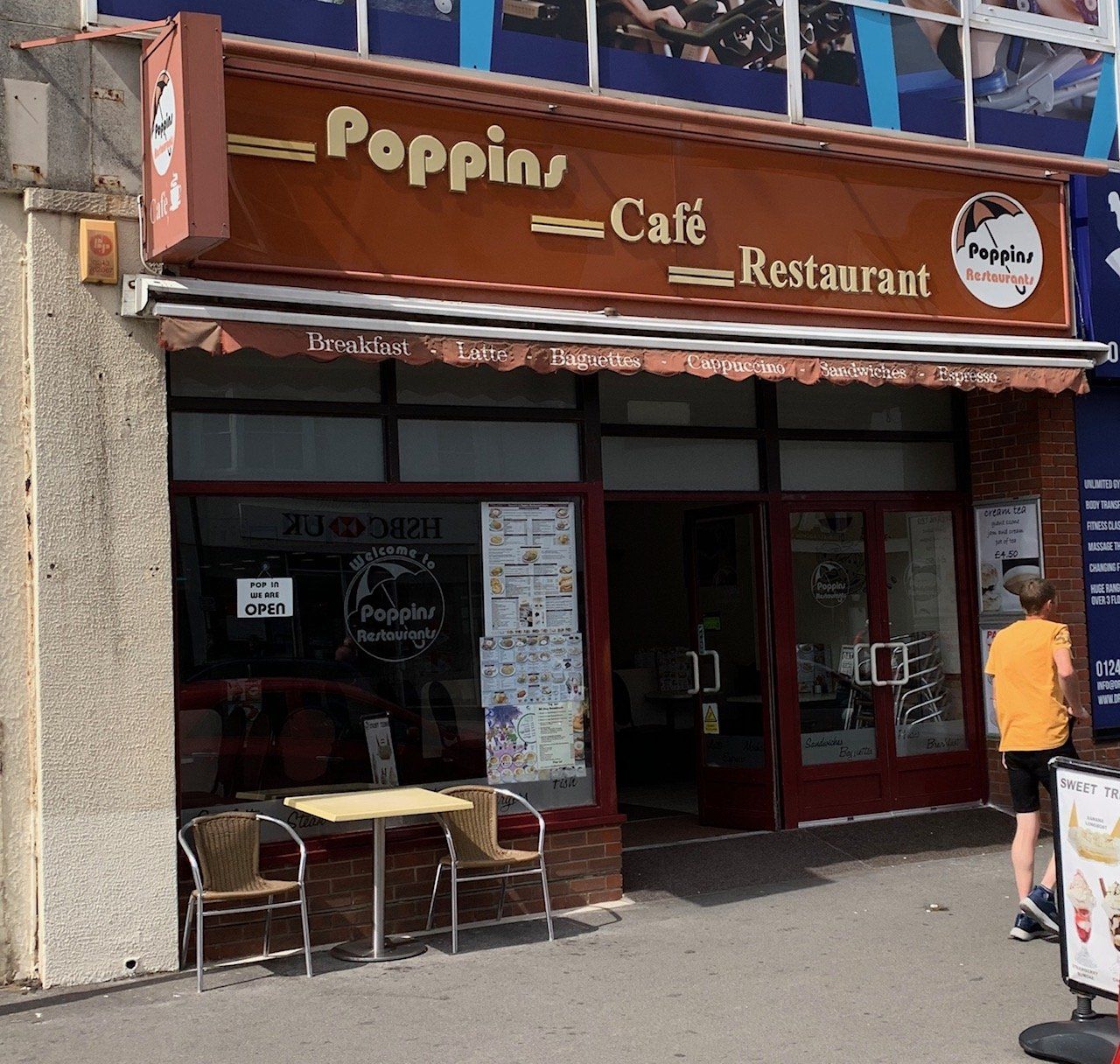 Popin Café Restaurant storefront with red doors, outdoor seating, and a person walking by