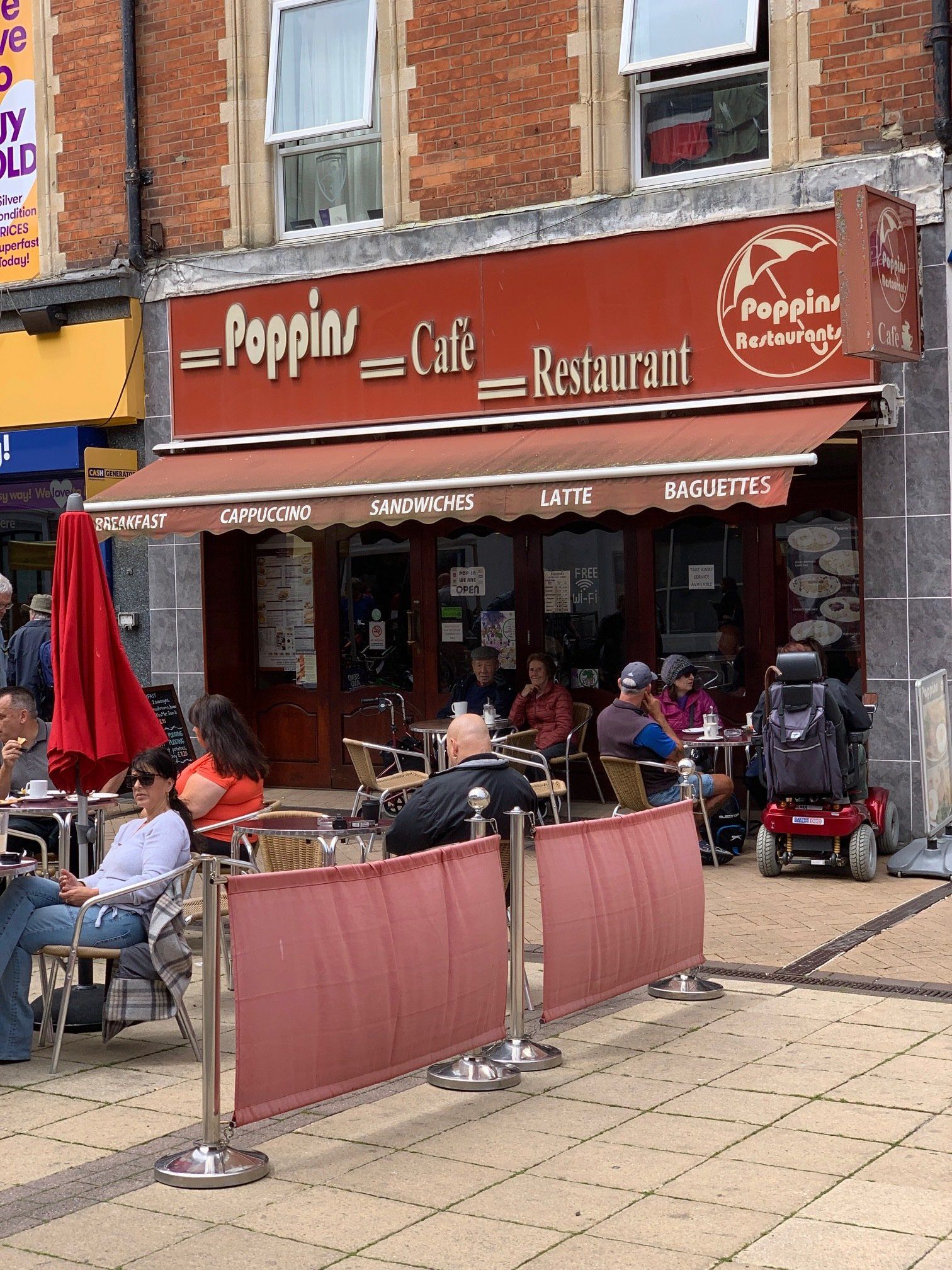 Outdoor cafe terrace at Poppin Cafe Restaurant with red awning and seated patrons on a sidewalk.