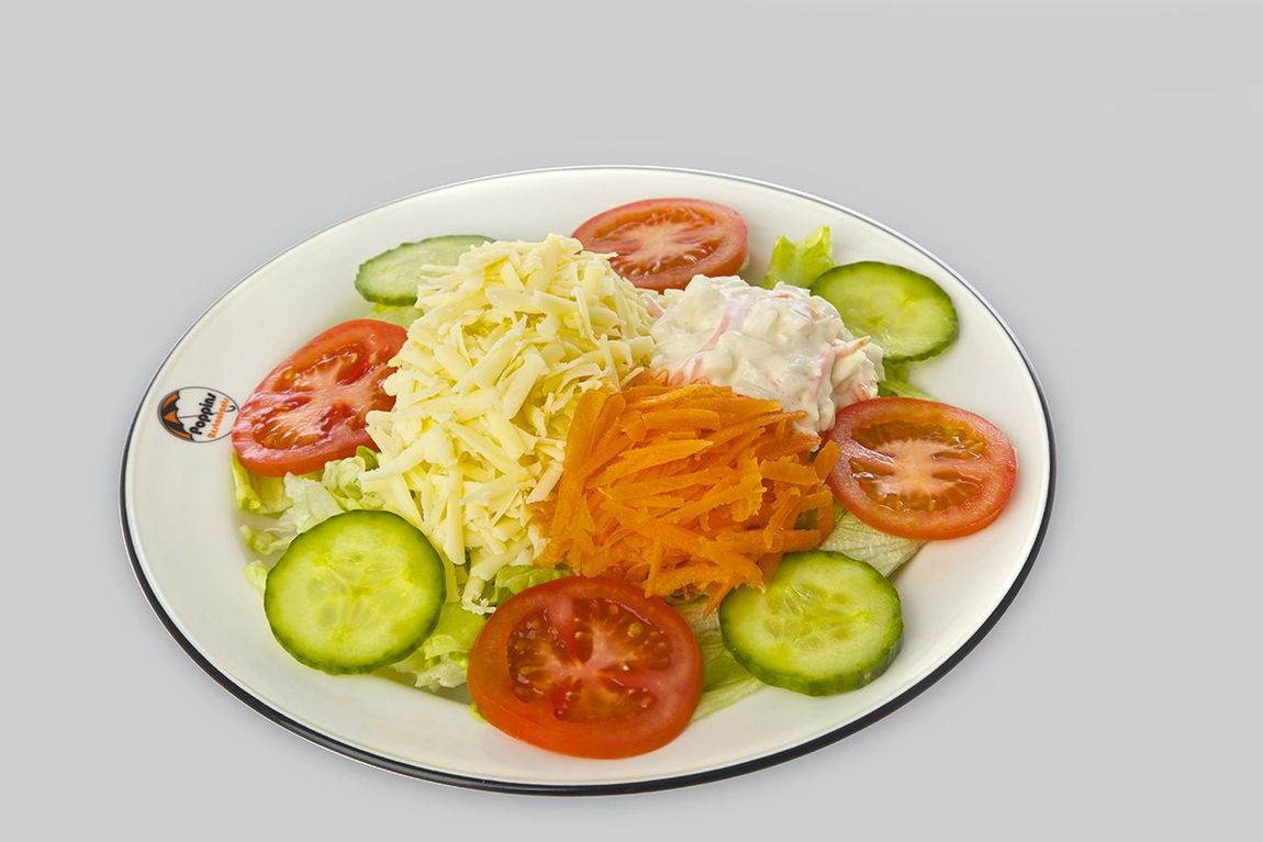 Plate of mixed salad with lettuce, carrots, tomatoes, cucumbers, and a dollop of cream on a white plate