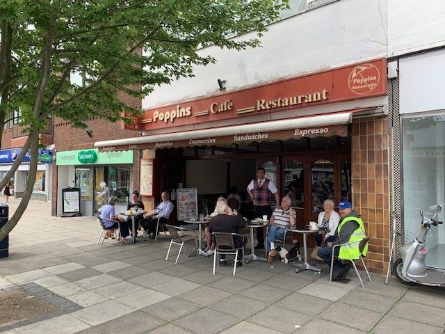 Outdoor café with people seated at tables outside a restaurant on a tree-lined sidewalk.