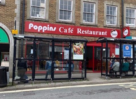Poppin Café Restaurant storefront with red signage, glass windows, and outdoor seating on a city street