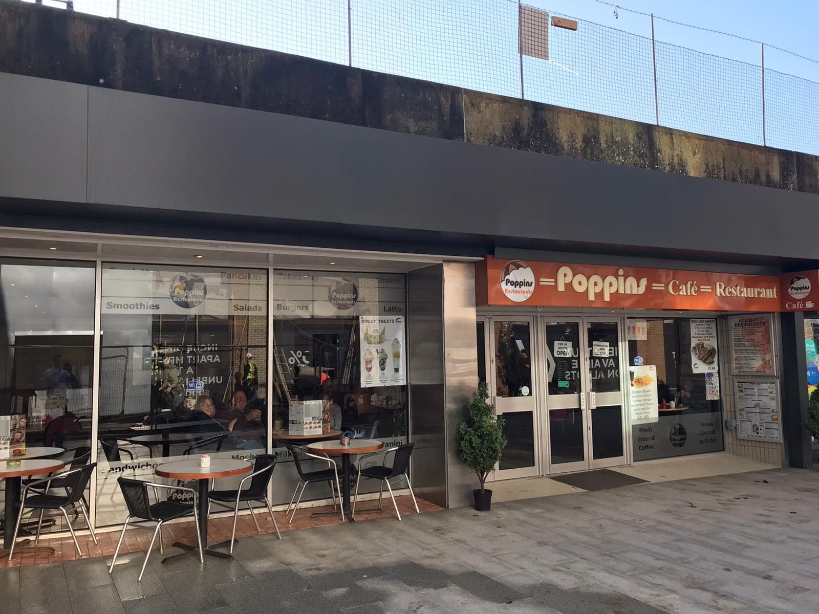 Outdoor café storefront with tables and chairs beside a red sign reading “Poppin”