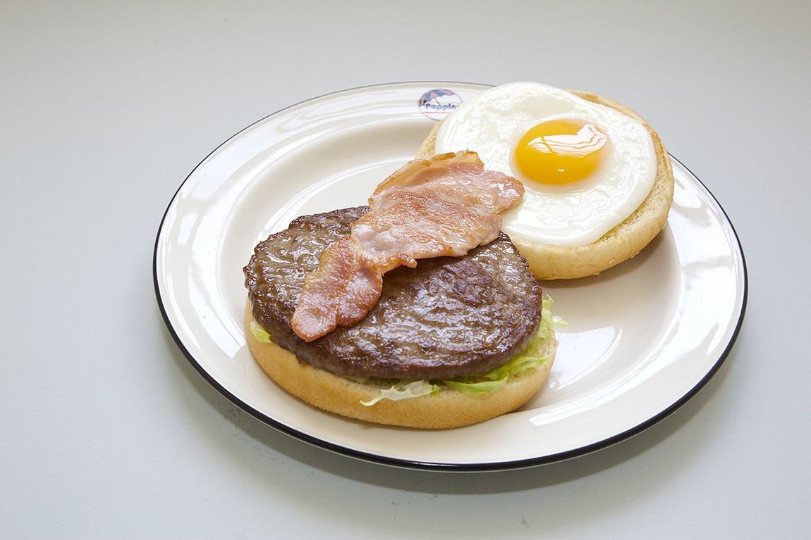 Plate with a hamburger patty, bacon, and two fried eggs on a white plate