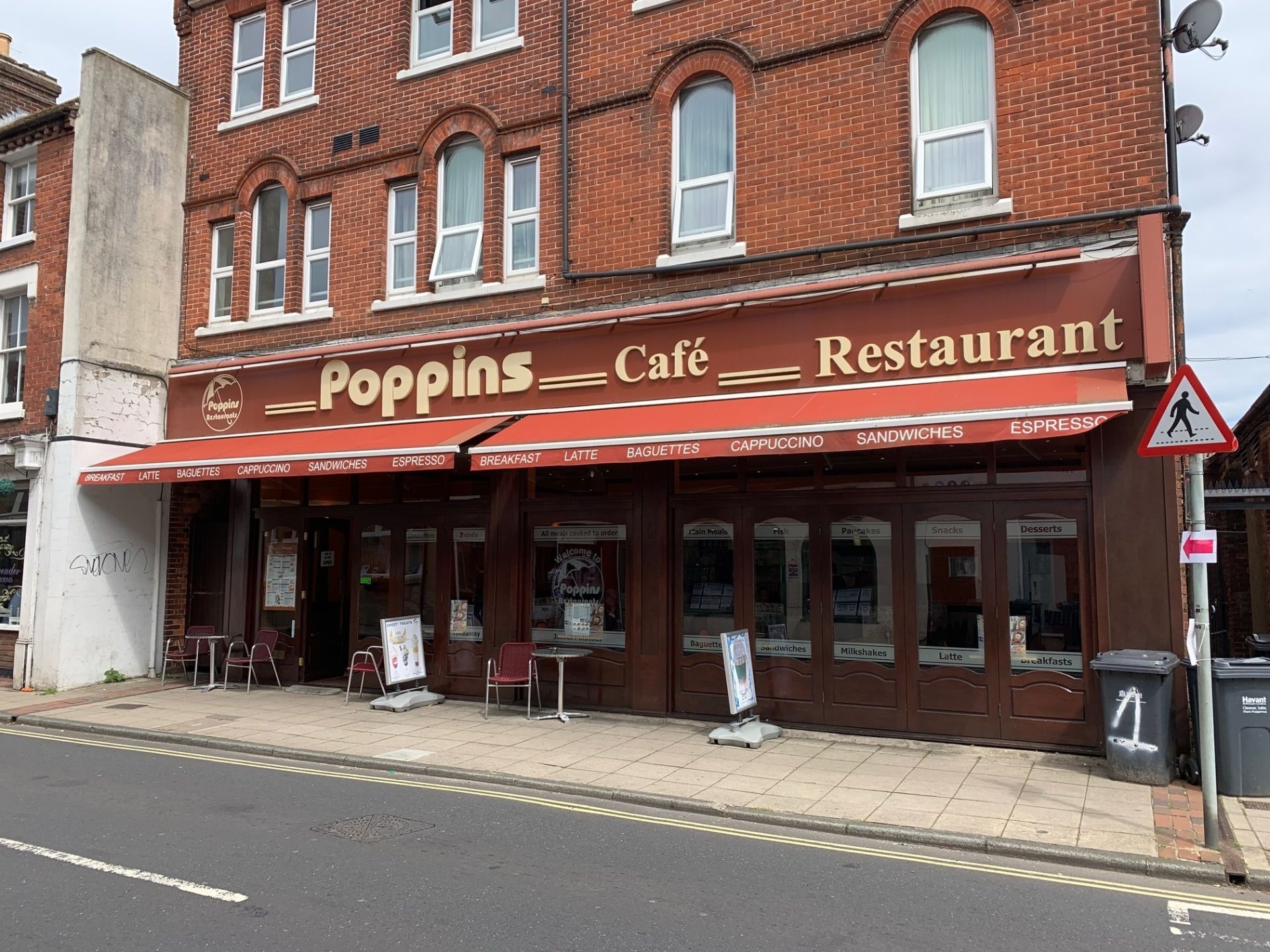 Red-brick storefront with a red awning reading “Poppins Café Restaurant” on a street corner