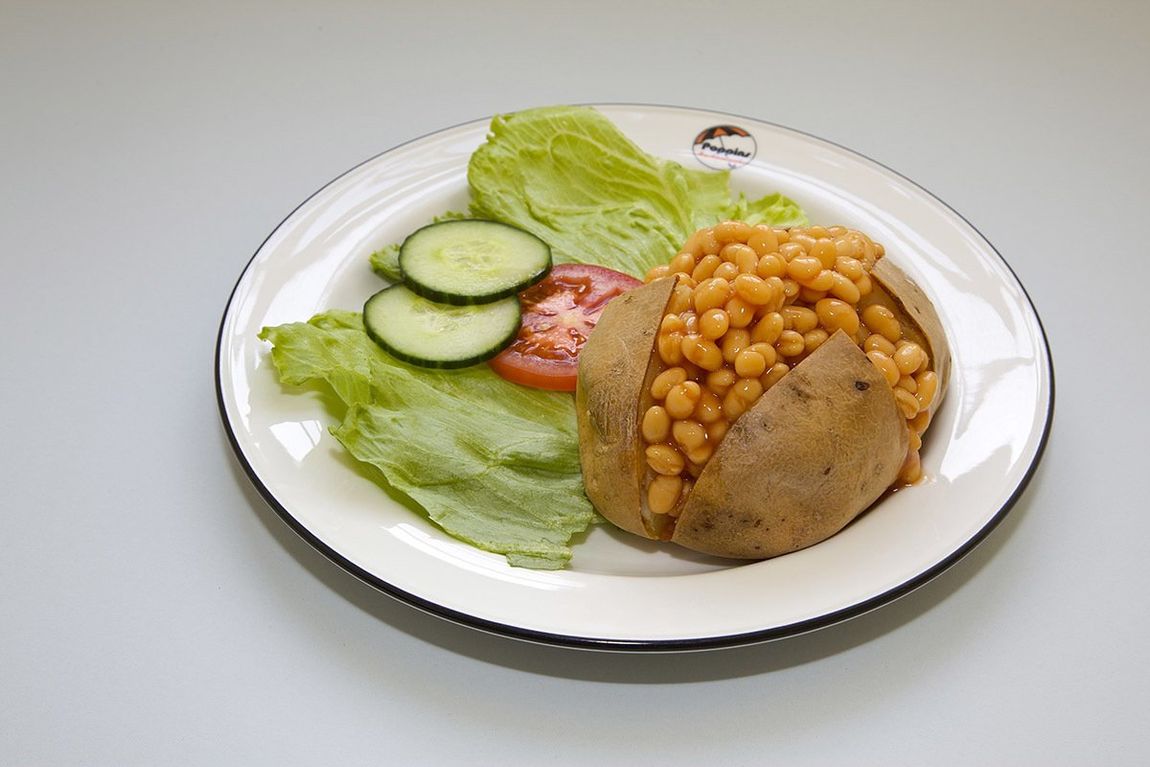 Baked potato topped with chickpeas on a white plate with lettuce, cucumber slices, and tomato wedge