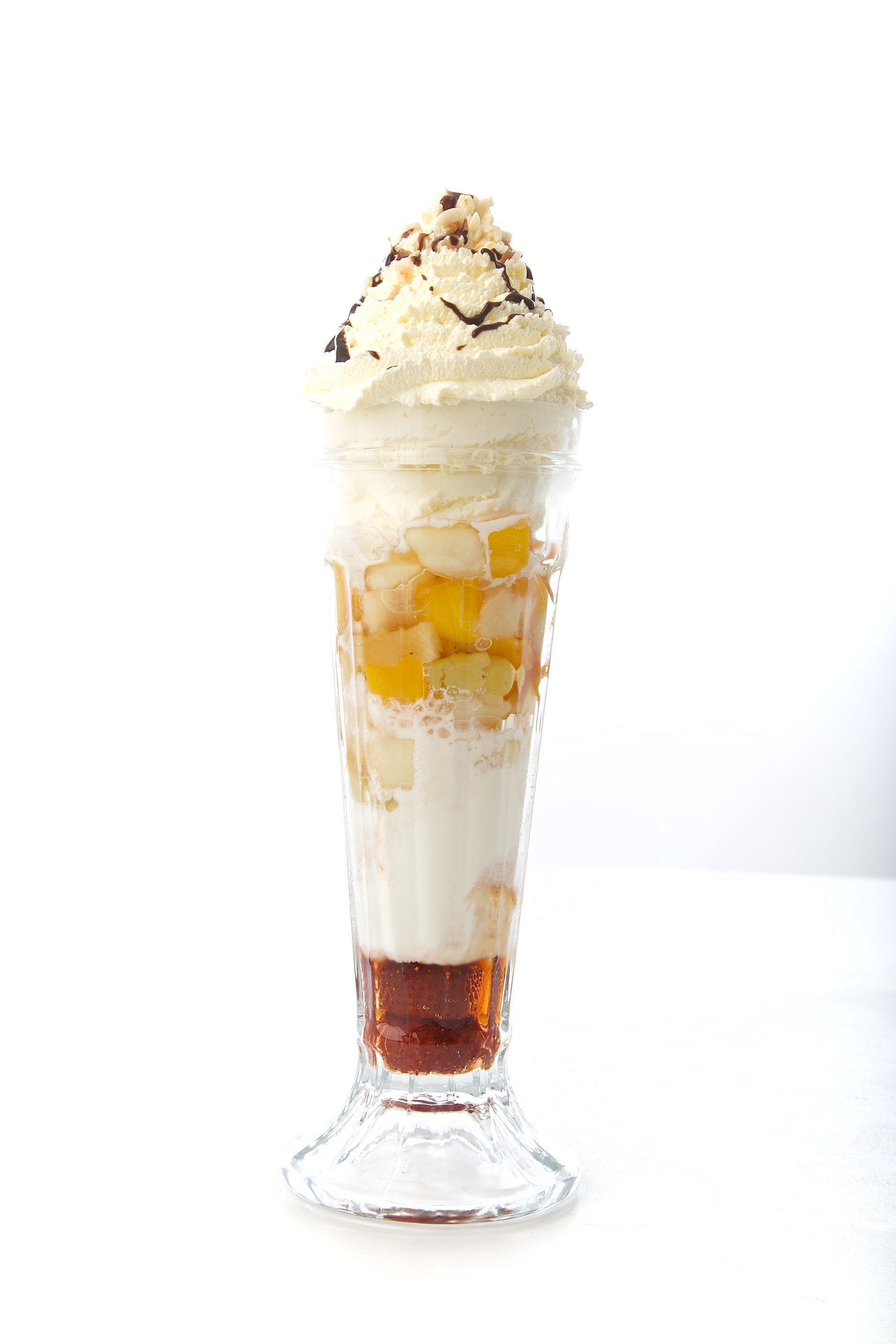 Tall dessert parfait glass with layered vanilla cream, fruit pieces, caramel, and whipped cream topped with nuts