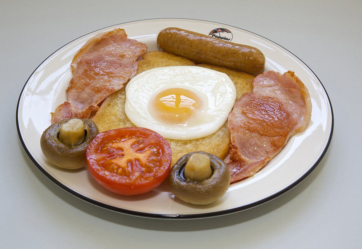 Breakfast plate with fried egg, sausage, bacon, tomato, and mushrooms on a white dish