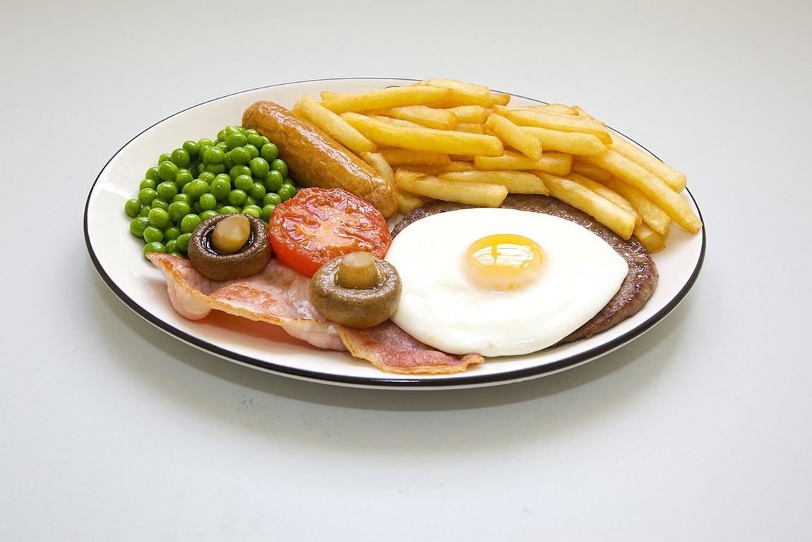 Breakfast plate with eggs, bacon, peas, mushrooms, tomato, and fries