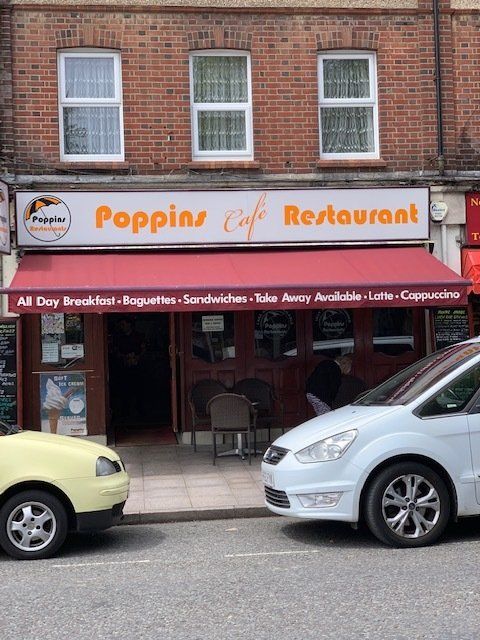 Storefront of Poppin’s Café Restaurant with orange signage, brick facade, and parked cars outside